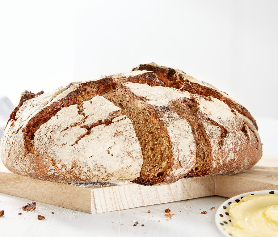 Ein Laib Brot auf einem Holzbrett neben einem Teller Butter.