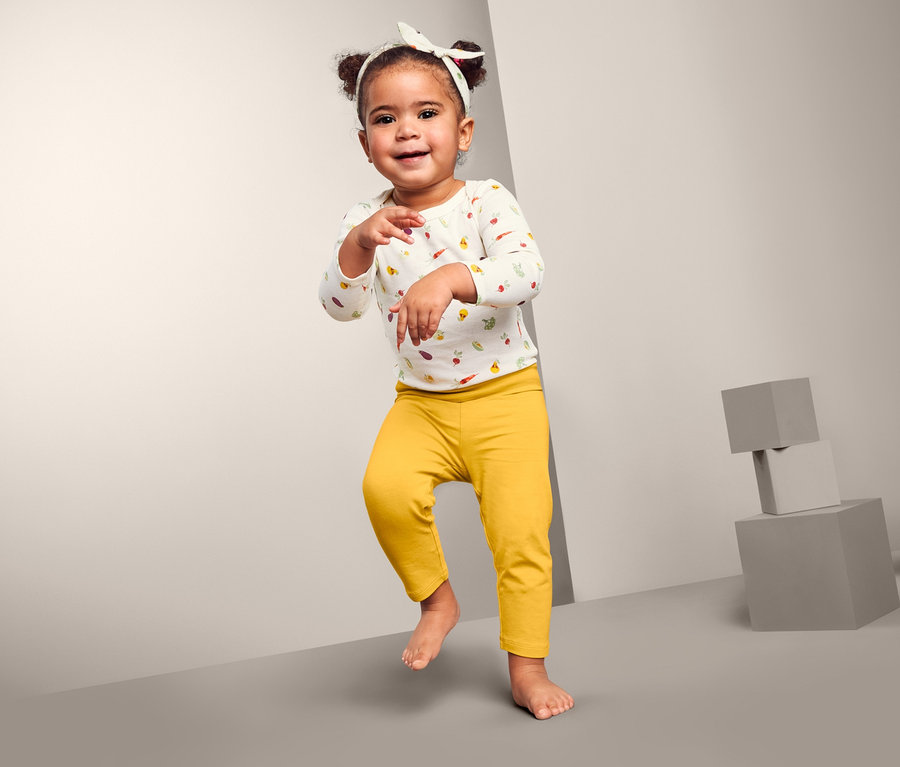 Lächelndes kleines Mädchen tanzt und trägt eine 3-teilige Baby-Kombi.