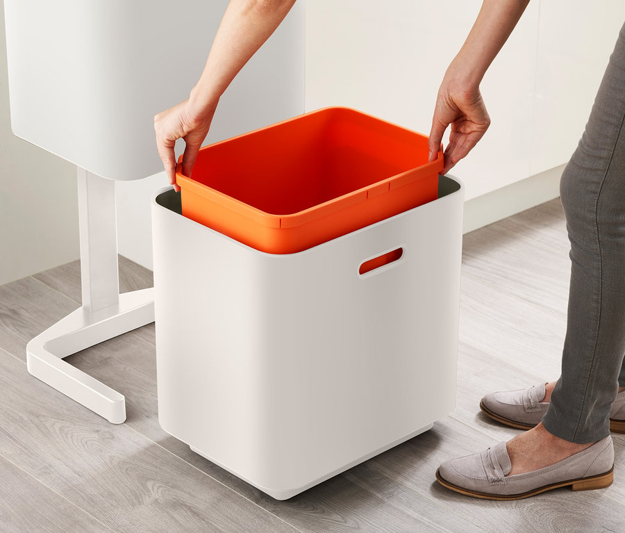 Eine Frau setzt einen orangefarbenen Behälter in einen Joseph Joseph Recycling-Abfalleimer.