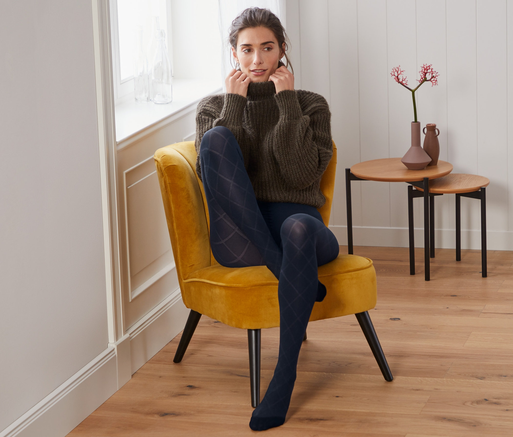 Frau sitzt im Sessel und trägt eine Feinstrumpfhose mit Karo-Struktur.