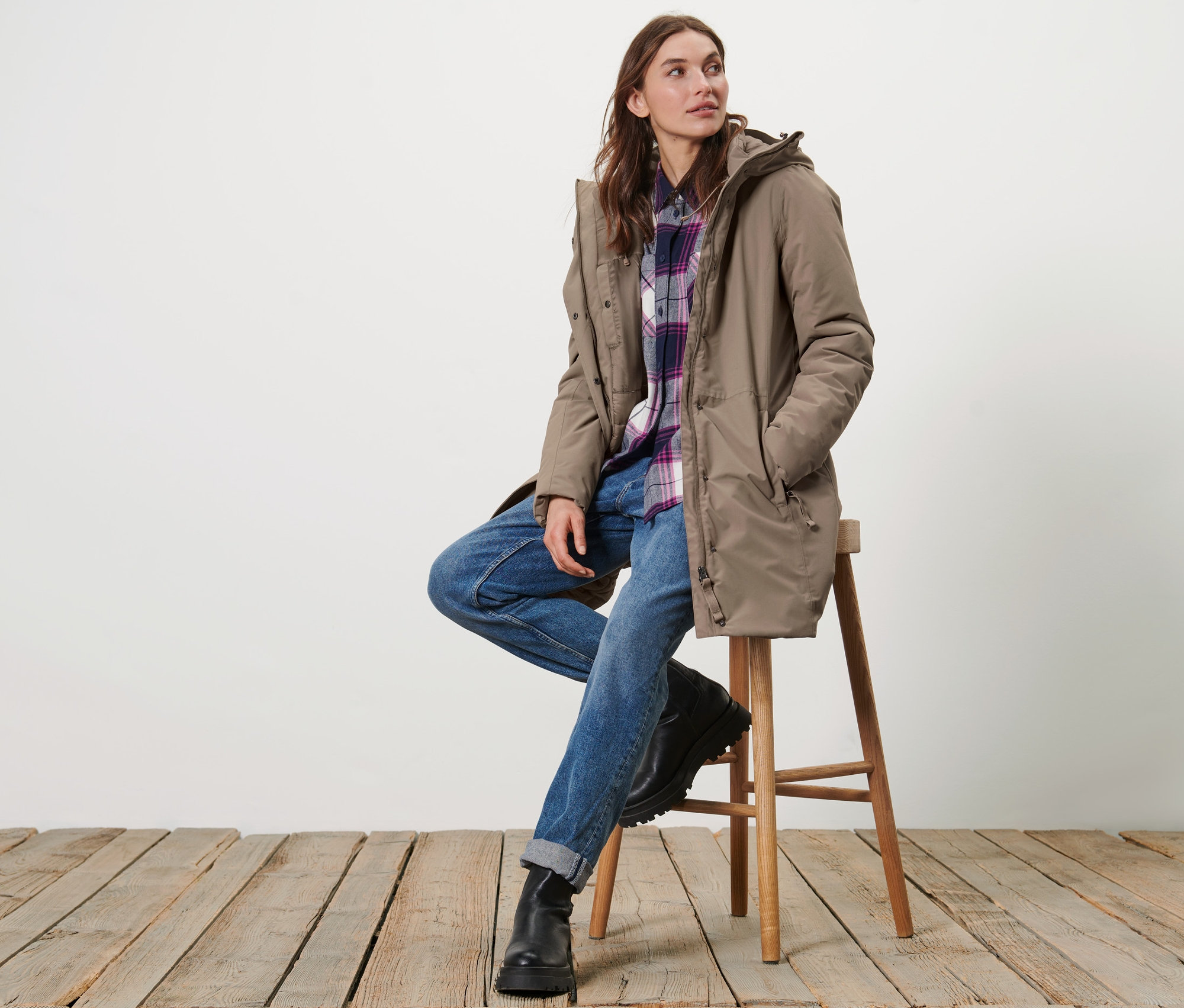 Frau sitzt auf einem Hocker und trägt einen beigen Thermo-Mantel.