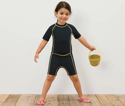 Mädchen im Kinder-Neoprenanzug hält gelben Eimer.
