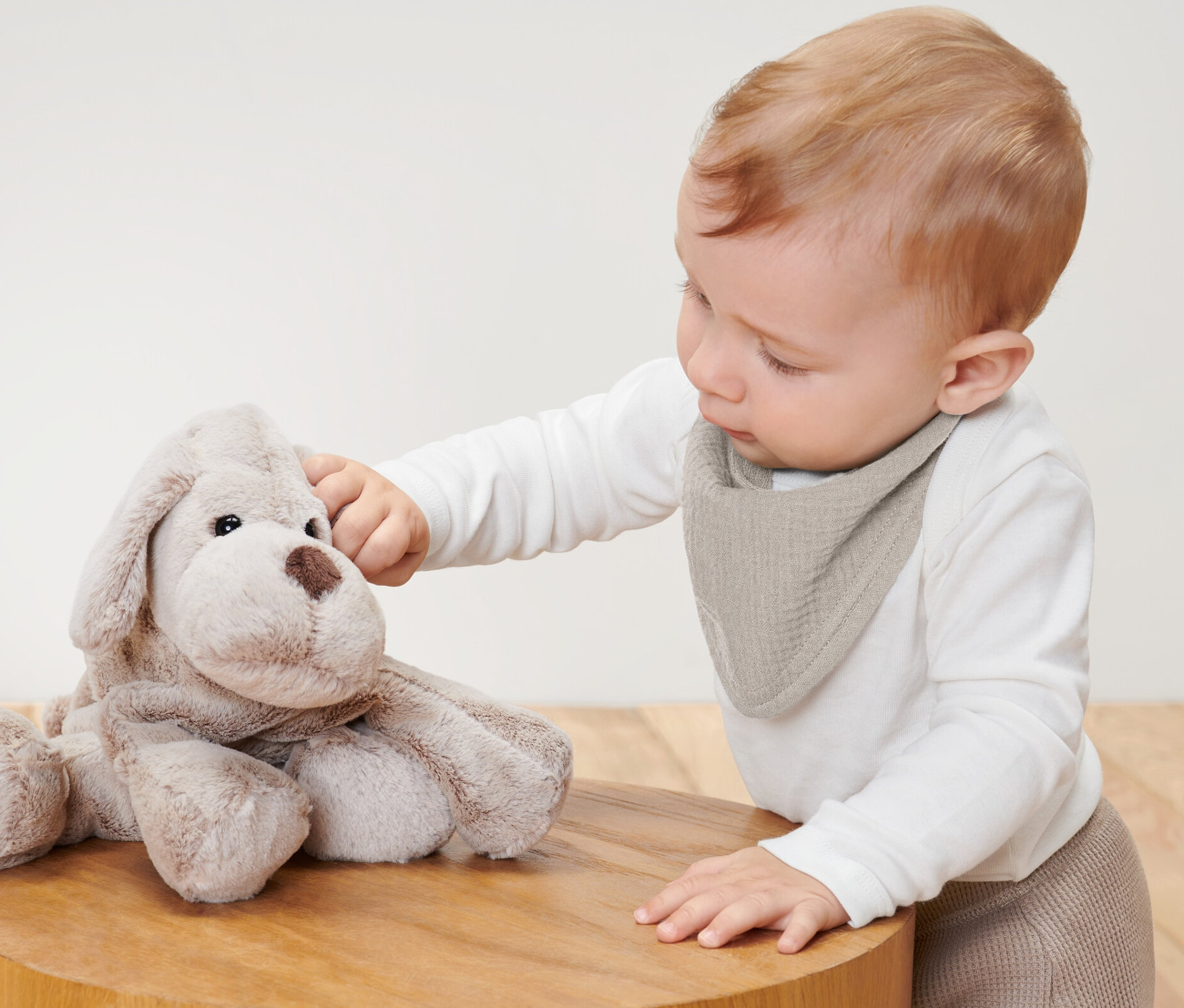 Baby berührt Plüschhund und trägt 2 Baby-Musselin-Halstücher.