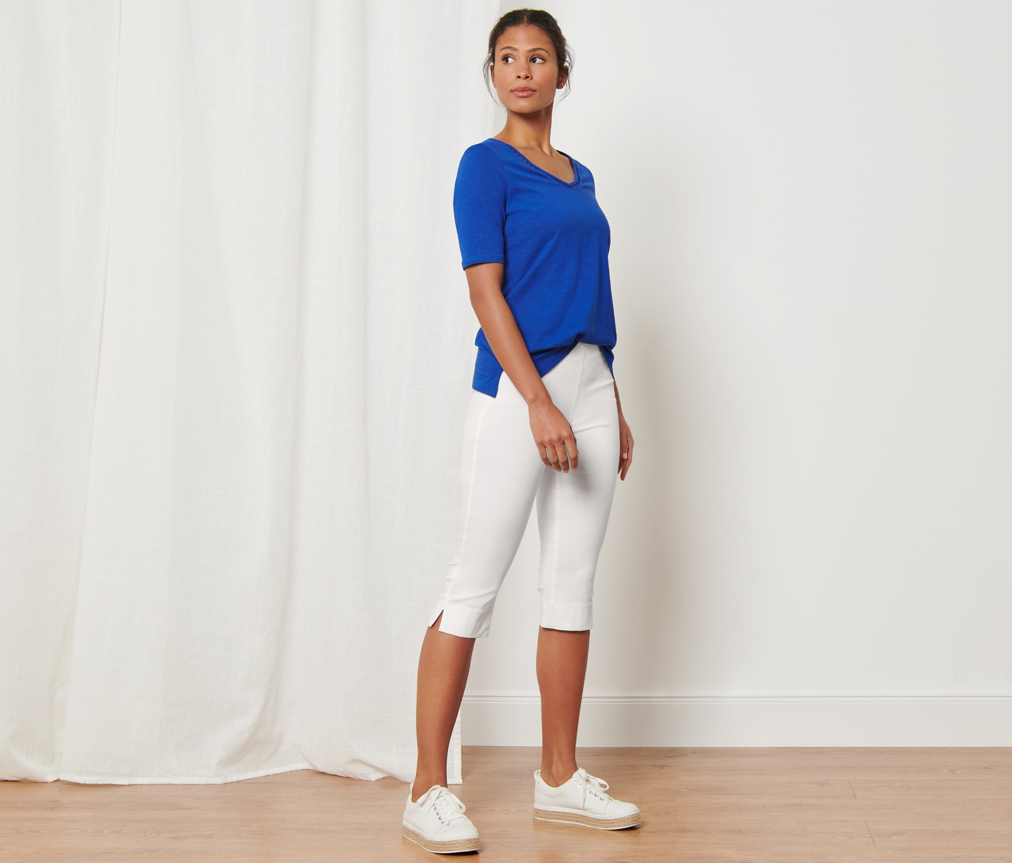 Frau steht in weißer 3/4-Stretchhose und blauem T-Shirt.