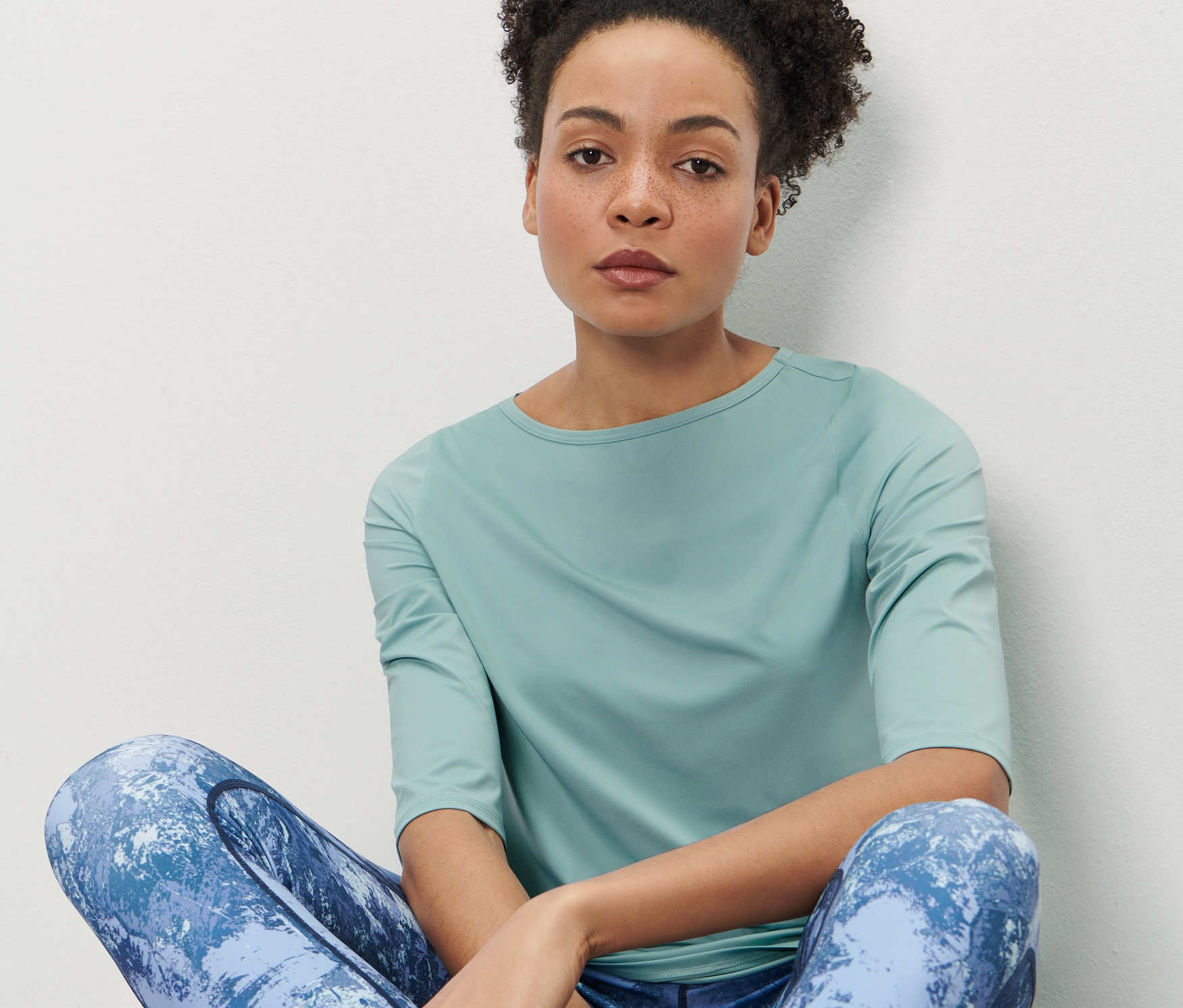 Frau sitzt und trägt ein mintfarbenes Funktionsshirt mit 3/4-Ärmeln.