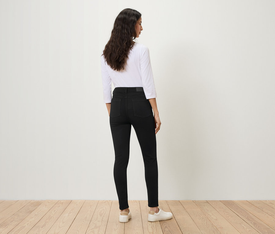 Eine Frau steht mit dem Rücken zur Kamera und trägt schwarze Jeans und ein weißes Hemd.