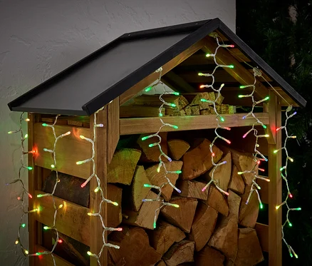 Holzschuppen gefüllt mit Holzscheiten, dekoriert mit bunten Lichtern.