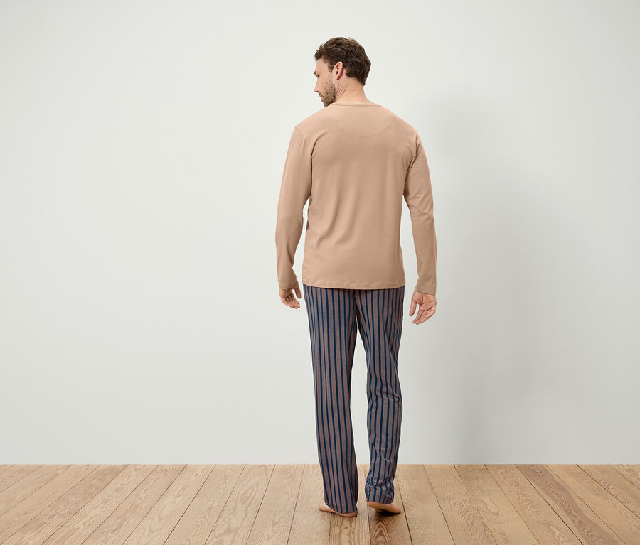 Mann mit beigem Langarmshirt und blau-grau gestreiften Hosen steht mit dem Rücken zur Kamera.