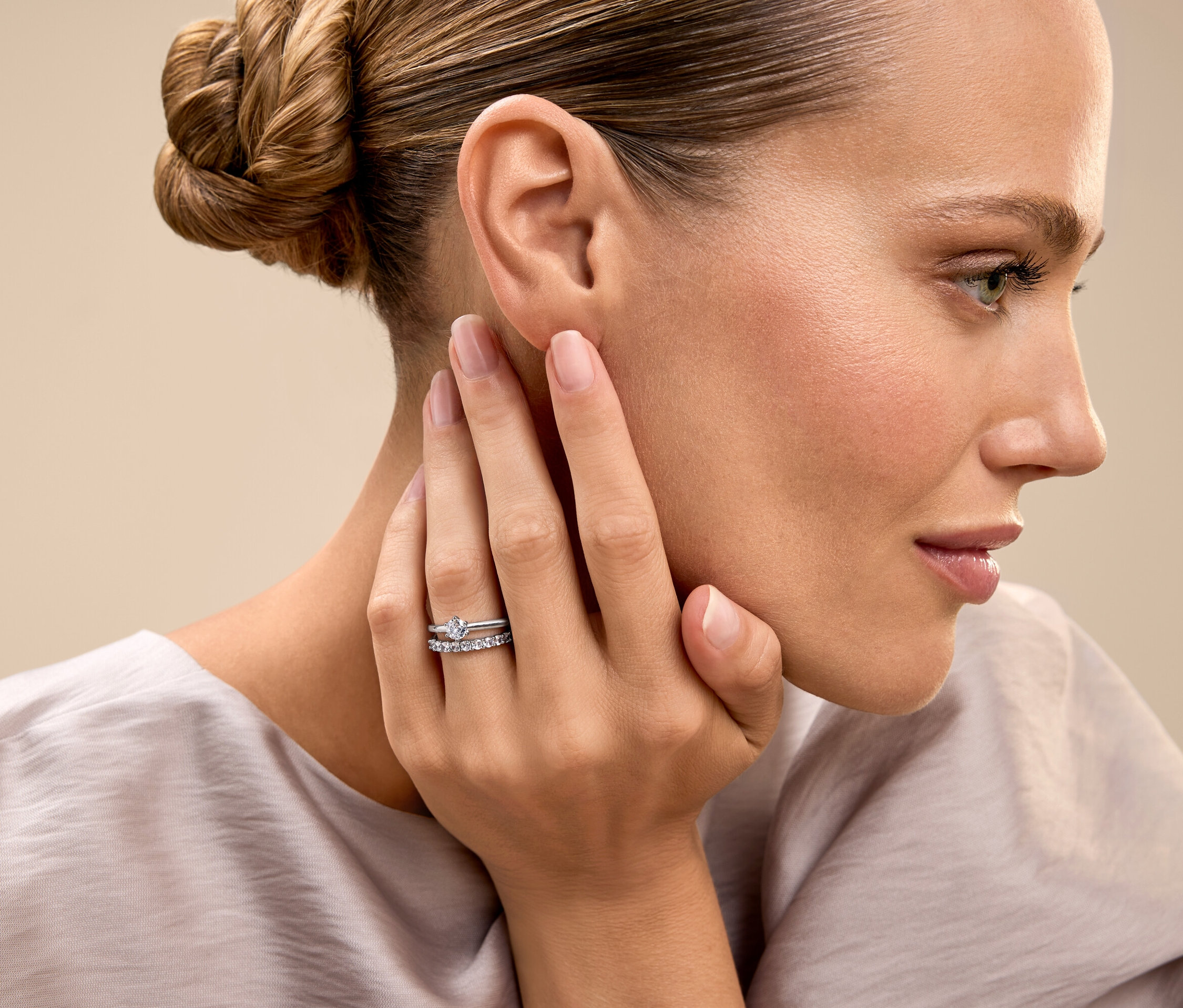 Frau mit hochgesteckten Haaren berührt ihr Gesicht und zeigt einen Ring.