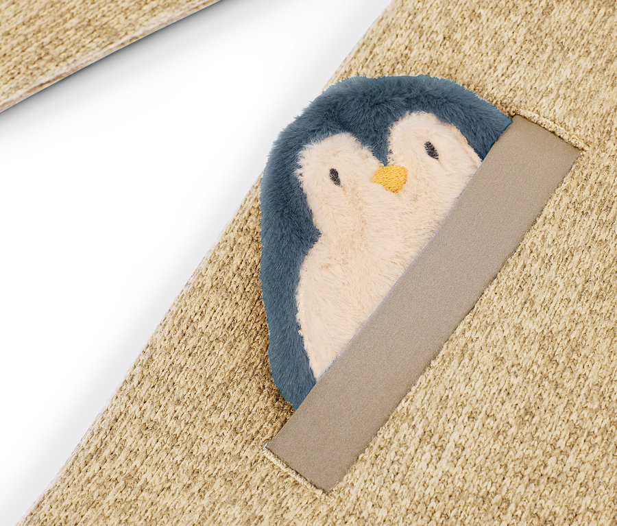 Detail eines beigen Teppichs mit aufgenähtem Plüschpinguin.