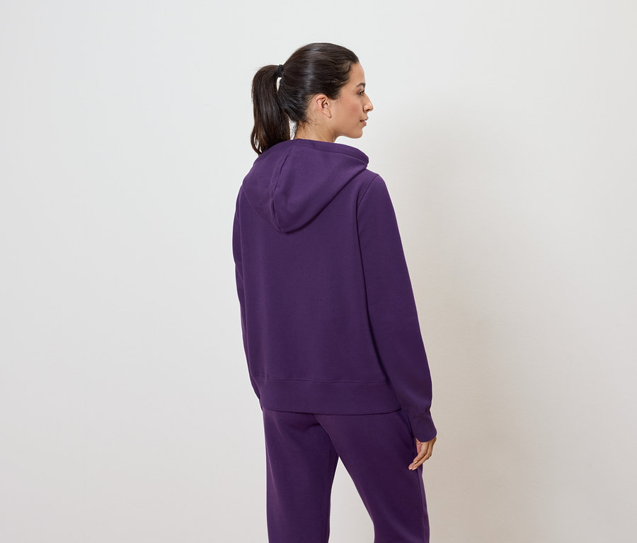 Frau mit dem Rücken zur Kamera trägt einen violetten Hoodie und eine Jogginghose.