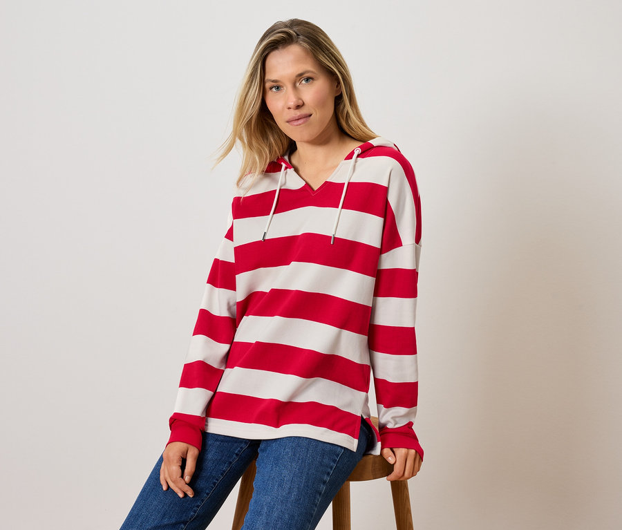 Eine Frau sitzt auf einem Hocker und trägt ein gestreiftes Kapuzenshirt und Jeans.