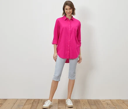 Frau steht und trägt eine lange Leinenbluse, pink.