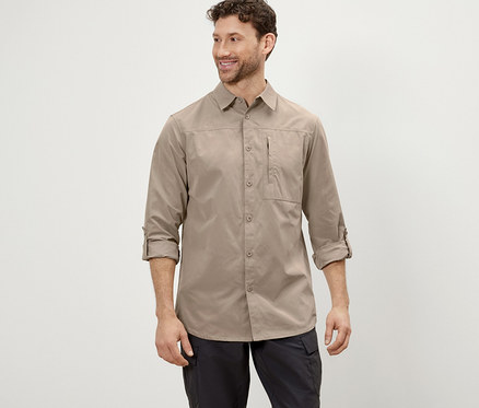 Ein Mann posiert in einem beigen Outdoorhemd mit Moskito-Schutz und einer schwarzen Hose.