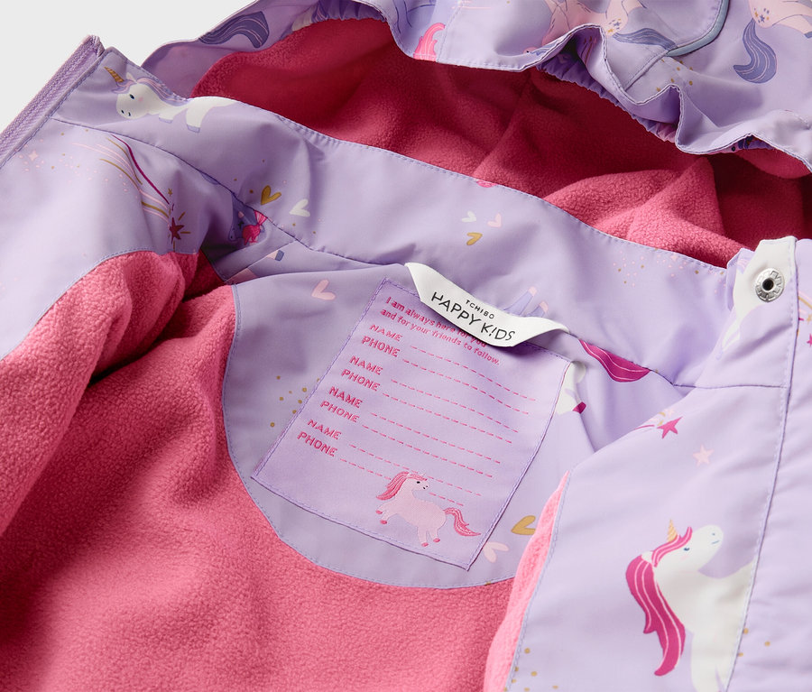 Nahaufnahme einer lila Kinderjacke mit Einhornmuster und rosa Fleecefutter. Ein Etikett mit "HAPPY KIDS" und Platz für Name/Telefon ist sichtbar.