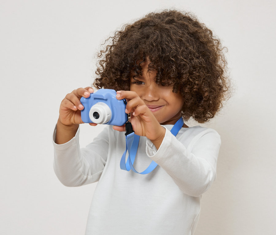 Kind mit lockigem Haar hält eine blaue Spielzeugkamera.