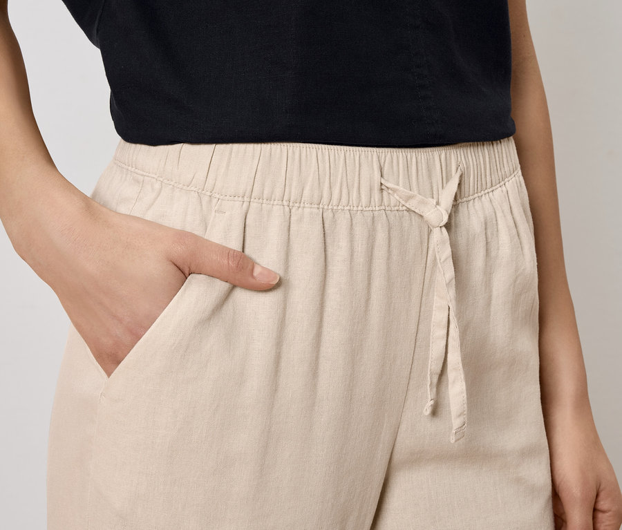 Frau mit Hand in der Tasche einer beigen Hose mit Kordelzug.