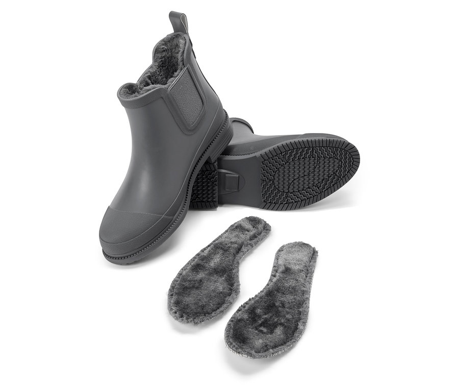Ein grauer Gummistiefel steht, ein weiterer liegt mit der Sohle nach oben, daneben zwei graue Einlegesohlen.