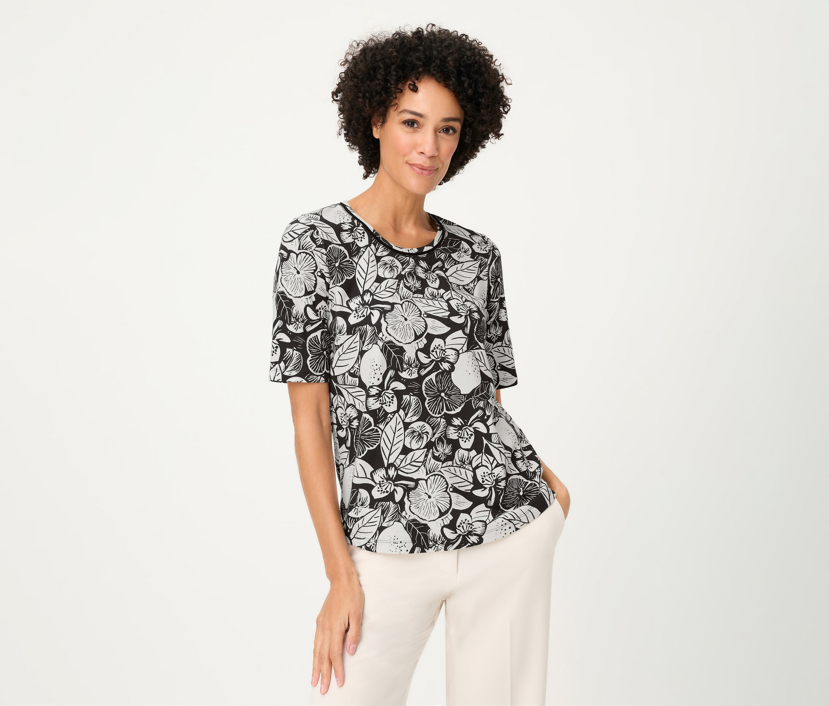 Frau mit lockigem Haar trägt ein Olsen Shirt mit Blumenmuster und helle Hosen.