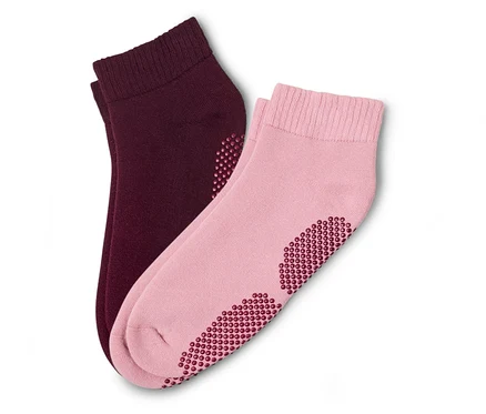 Ein Paar Socken, eine rosa und eine bordeauxrot, liegen übereinander. Beide haben Noppen an der Unterseite.