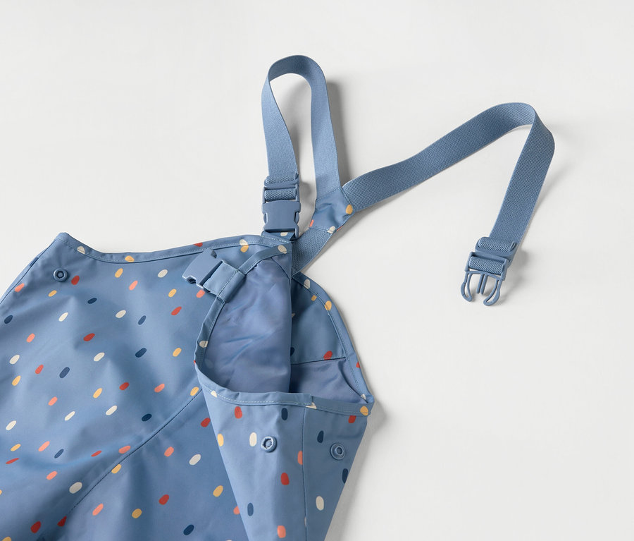 Blaue Kinderschürze mit bunten Punkten und blauen Trägern auf weißem Hintergrund.