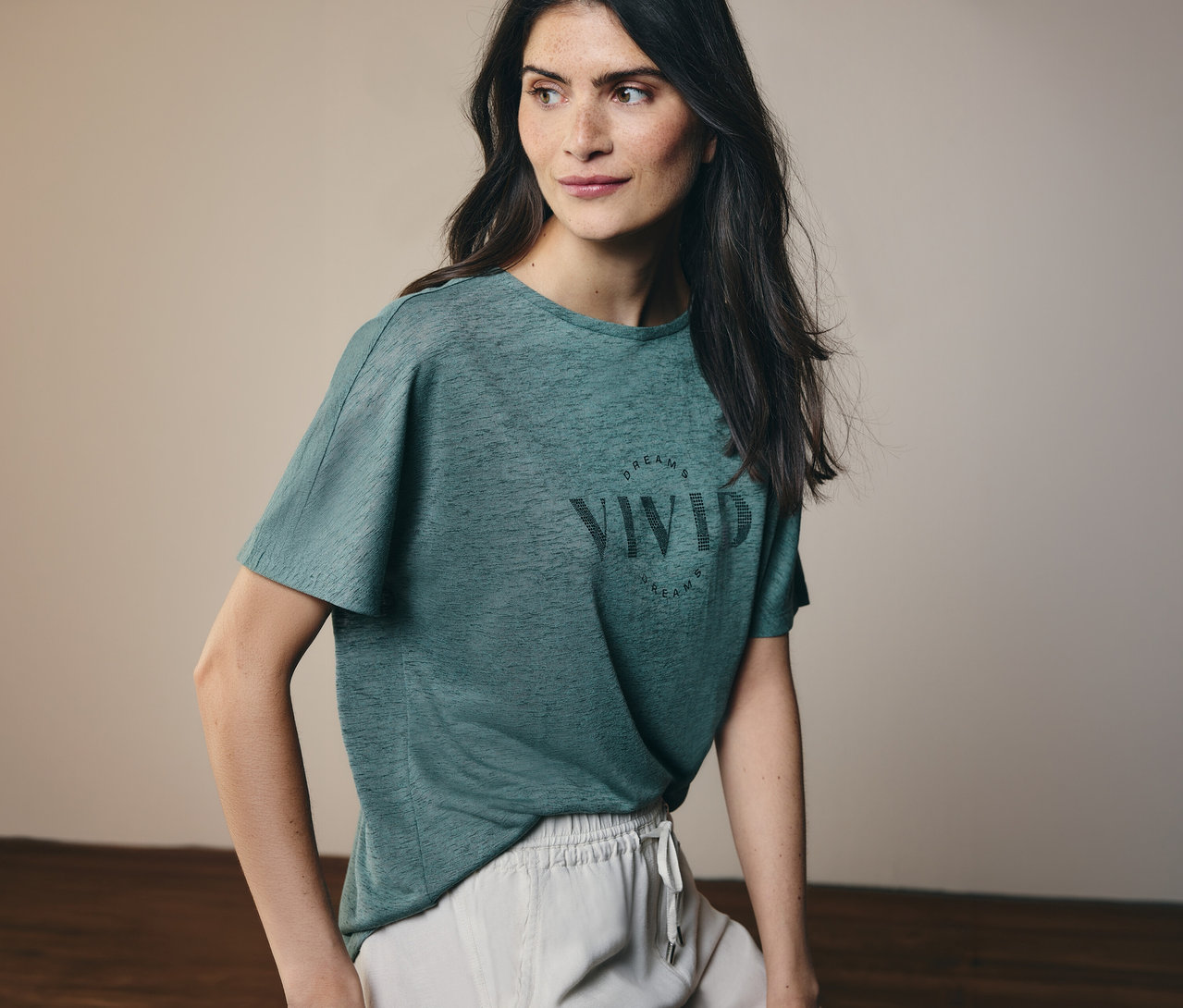 Frau mit langen, dunklen Haaren trägt ein grünes T-Shirt mit der Aufschrift "Vivid Dreams" und helle Shorts.