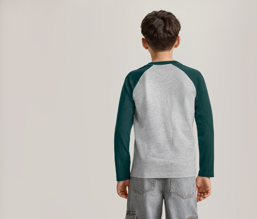 Ein kleiner Junge von hinten, der ein langärmeliges Raglan-T-Shirt in Grau und Dunkelgrün sowie graue Shorts trägt.