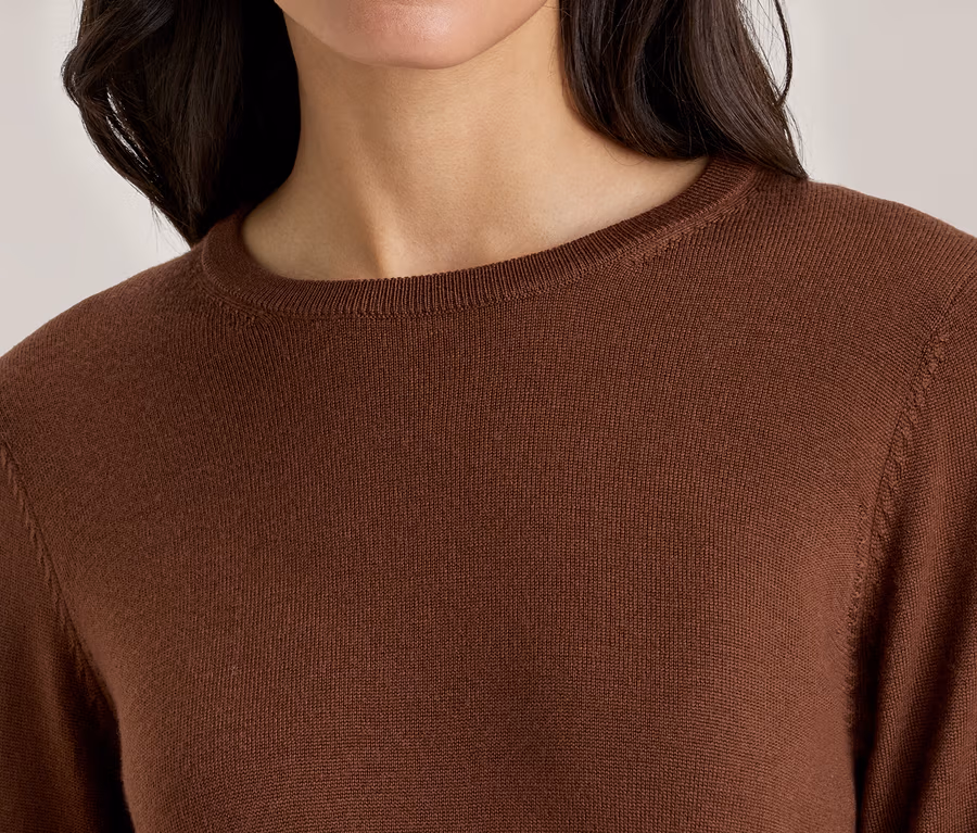 Frau trägt einen braunen, langärmeligen Pullover mit Rundhalsausschnitt.