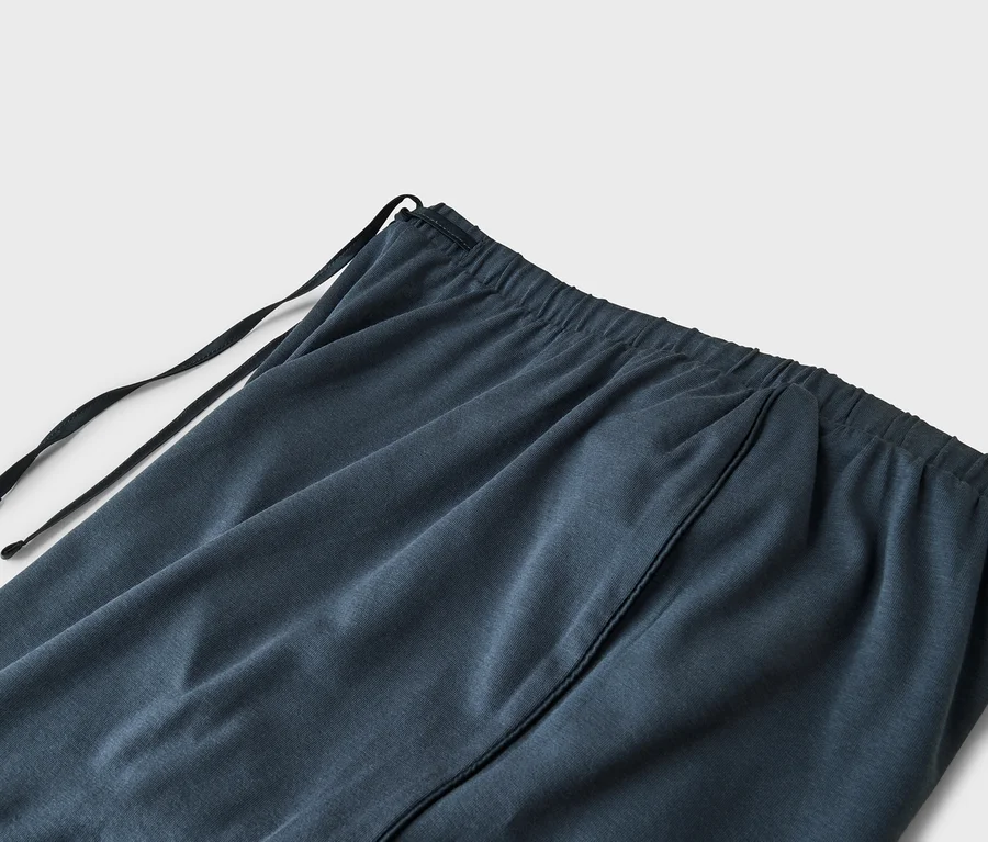 Nahaufnahme eines dunkelblauen oder grauen Stoffes mit elastischem Bund und schwarzem Kordelzug. Eine vertikale Naht ist sichtbar.