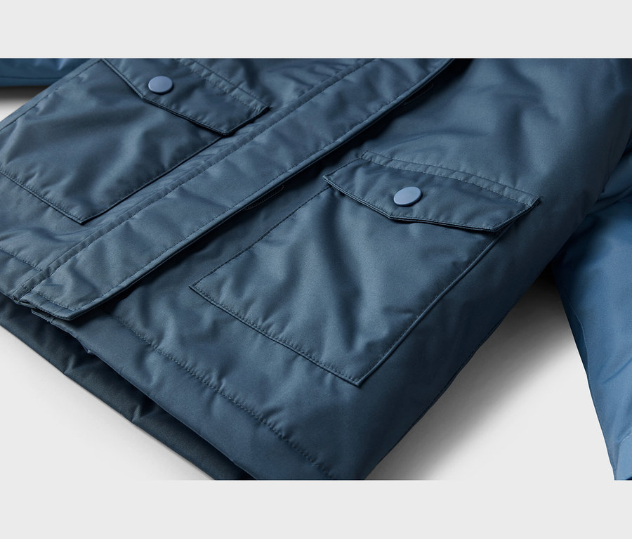 Nahaufnahme einer blauen Jacke, die zwei Pattentaschen mit passenden blauen Knöpfen zeigt.