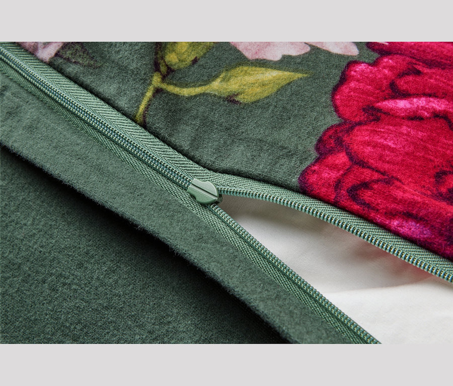Nahaufnahme eines grünen Stoffes mit Blumenmuster aus roten und rosa Blüten, mit einem teilweise geöffneten grünen Reißverschluss, dessen Schieber sichtbar ist und weißen Stoff darunter zeigt.
