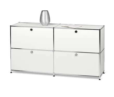 Ein weißes Sideboard Metall »CN3« mit 4 Klappfächern. Oben auf dem Schrank stehen eine silberne Vase und ein offenes Buch.