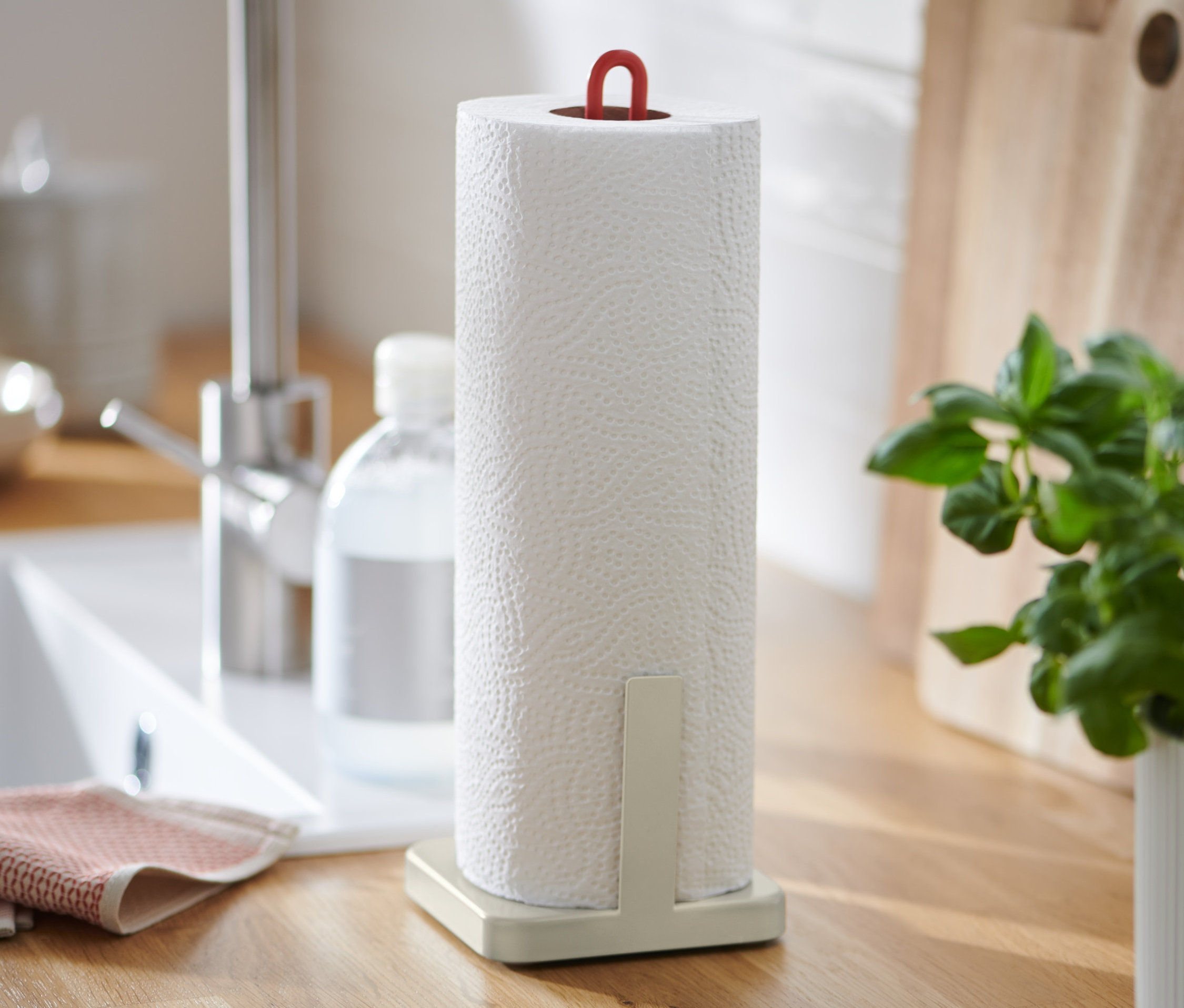 Auf einer Küchentheke stehen ein Küchenrollenhalter, ein Spülbecken, ein Seifenspender und ein Basilikumtopf.