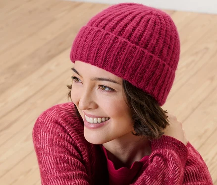 Lächelnde Frau trägt eine himbeerfarbene Strickmütze.