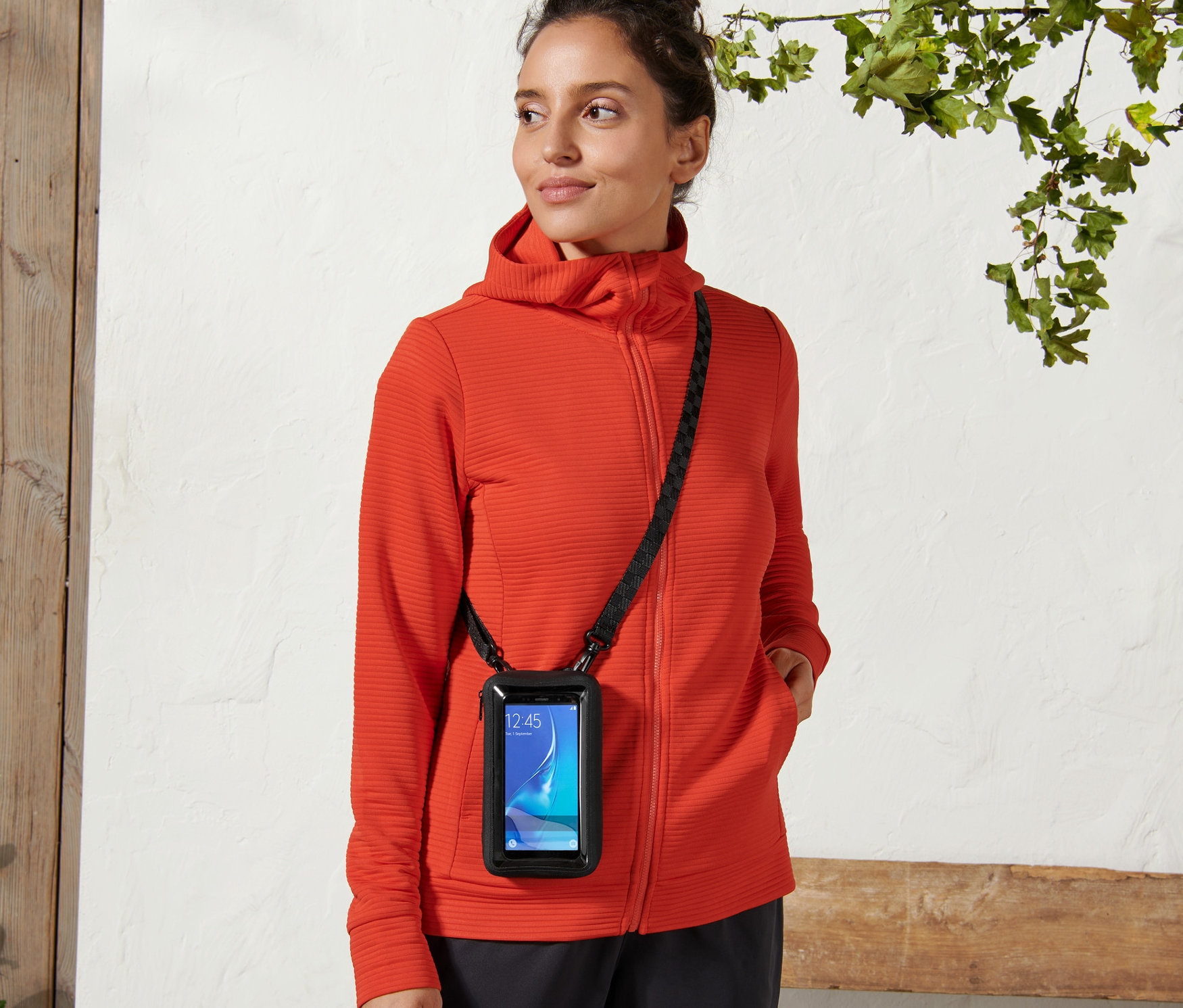 Frau trägt eine 2-in-1-Smartphonetasche mit einem schwarzen Riemen quer über den Körper.
