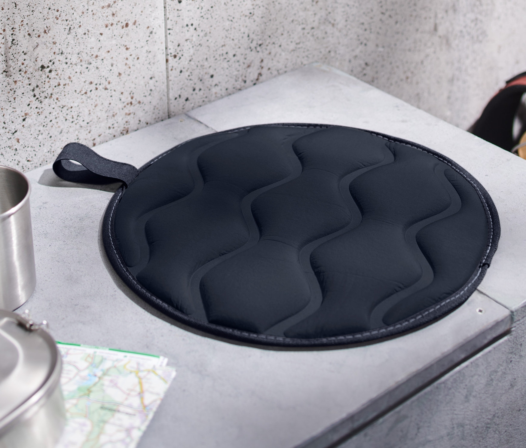 Ein faltbares Thermo-Sitzkissen liegt auf einer grauen Betonbank.