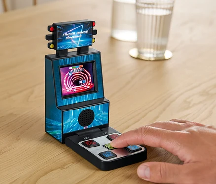 Eine Hand spielt Fingertanzmaschine auf einem Tisch neben einem Glas Wasser.