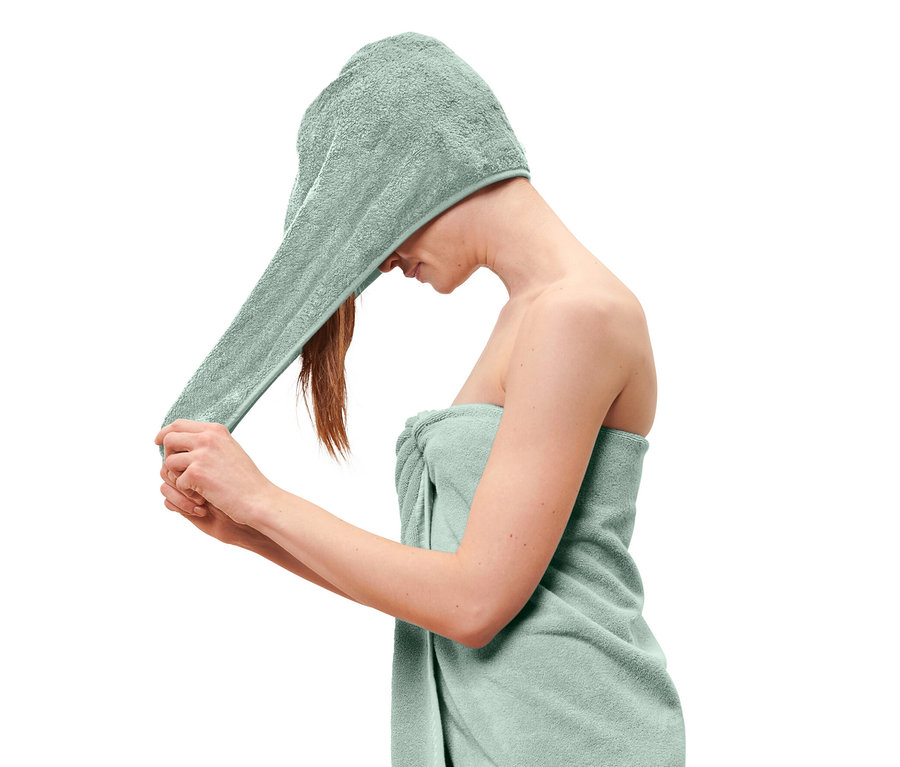 Frau legt ein hellblaues Turban-Handtuch auf ihren Kopf und hat ein hellblaues Handtuch um ihren Körper gewickelt.