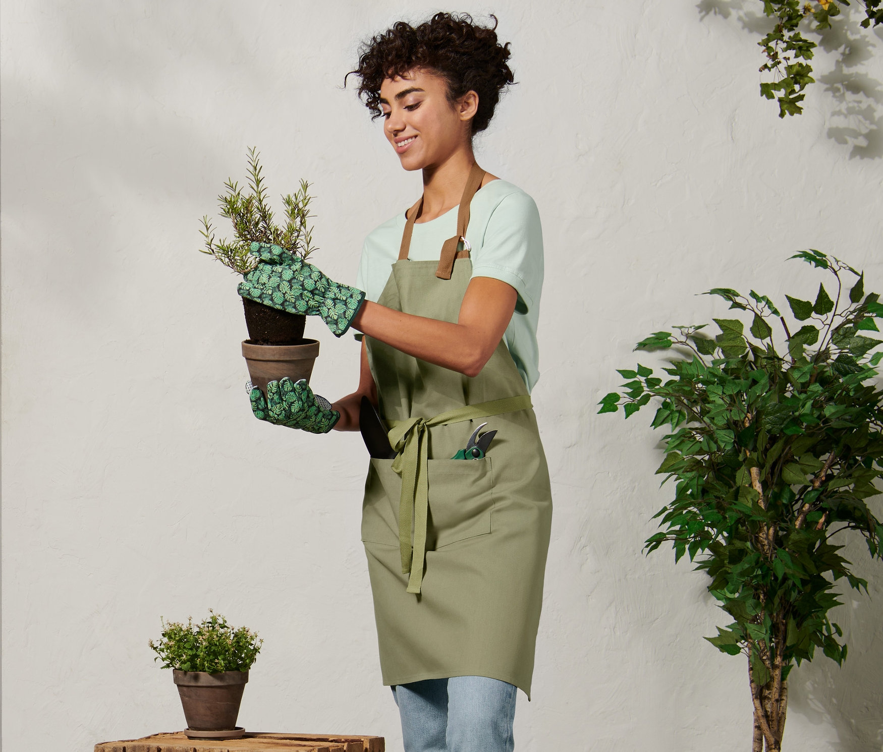 Frau mit Gartenschürze hält Blumentopf.