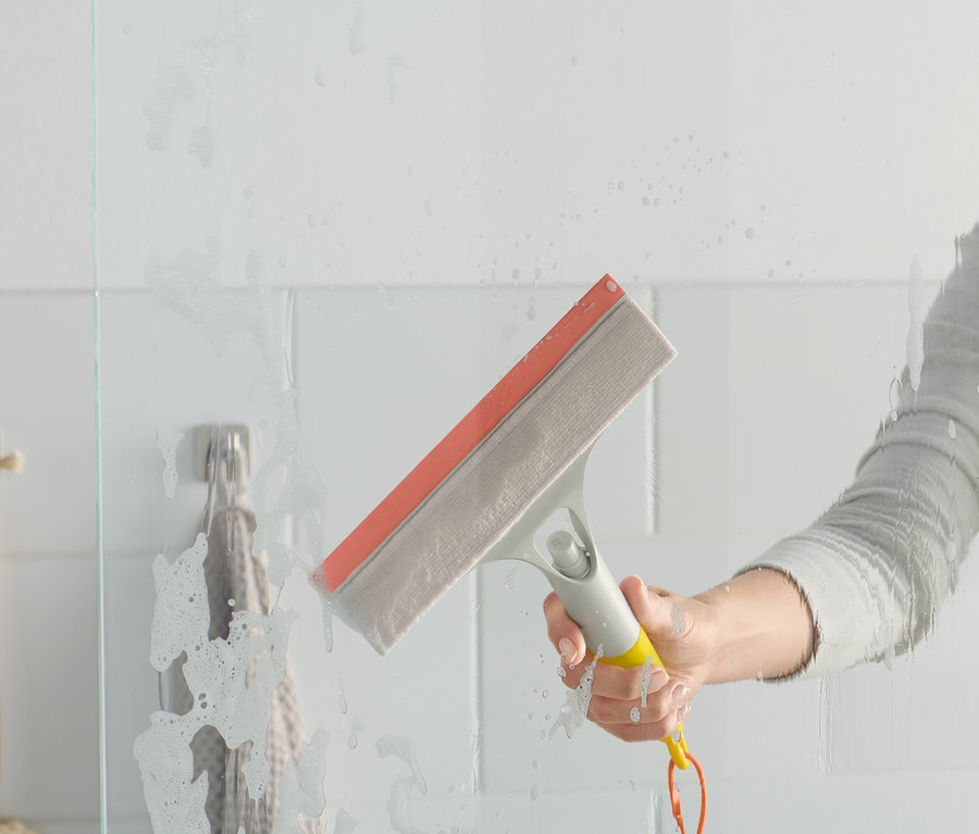 Eine Frau benutzt einen 3-in-1-Fensterwischer an einer Duschkabine aus Glas.