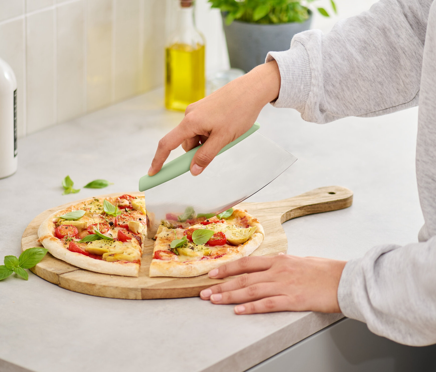 Eine Frau schneidet Pizza auf einem Holzbrett mit einem Pizza-und-Kräuter-Schneider.