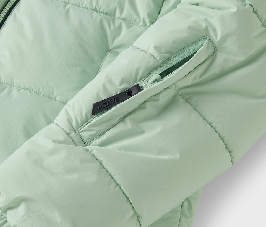 Detailaufnahme einer hellgrünen Steppjacke mit Reißverschlusstasche.