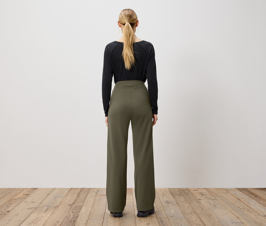 Frau mit Pferdeschwanz, von hinten gesehen, trägt ein schwarzes Langarmshirt und eine olivgrüne Hose.