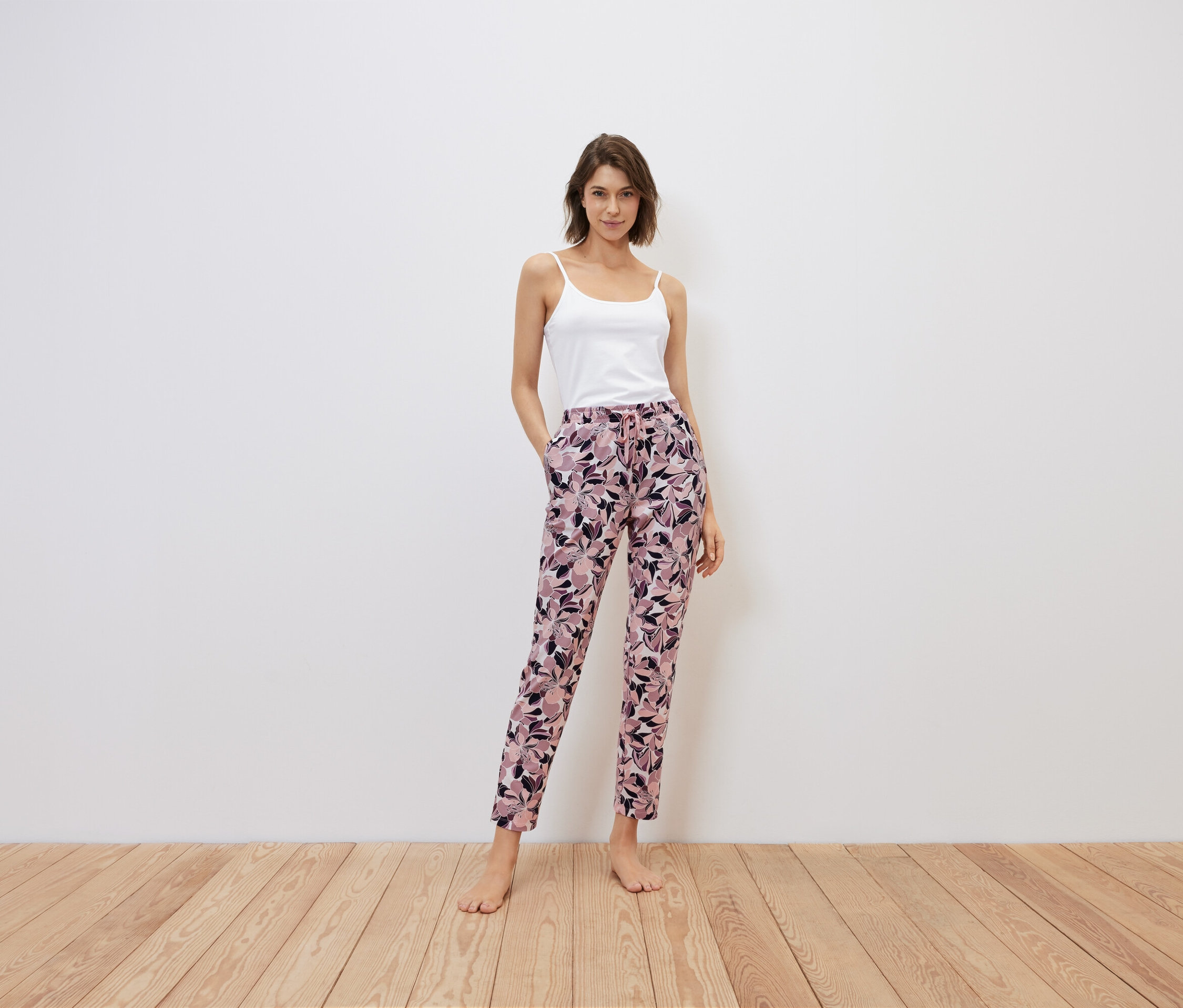 Frau steht mit Händen in den Taschen einer geblümten Hose, weißes Top.