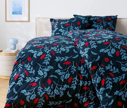 Bett mit dunkelblauer Bettwäsche mit roten und blauen Blättern.