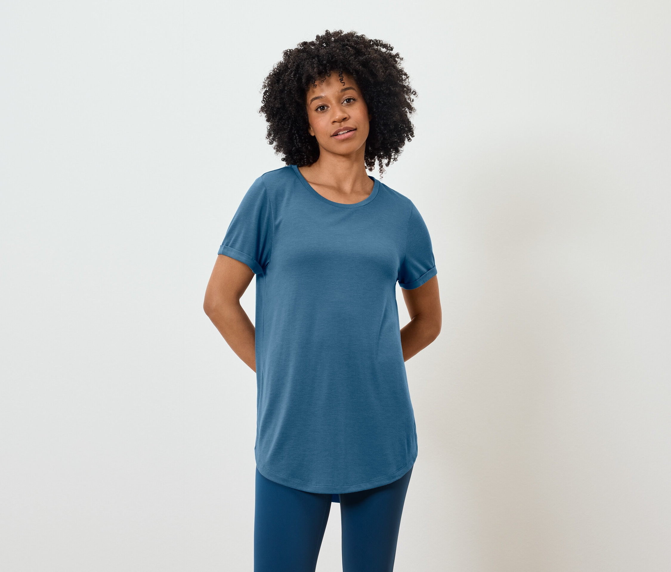 Eine Afroamerikanerin in einem blauen T-Shirt und Leggings steht vor einem weißen Hintergrund.