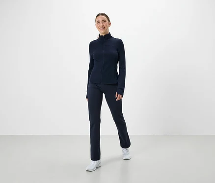 Eine Frau trägt ein marineblaues Sportoutfit und weiße Turnschuhe.