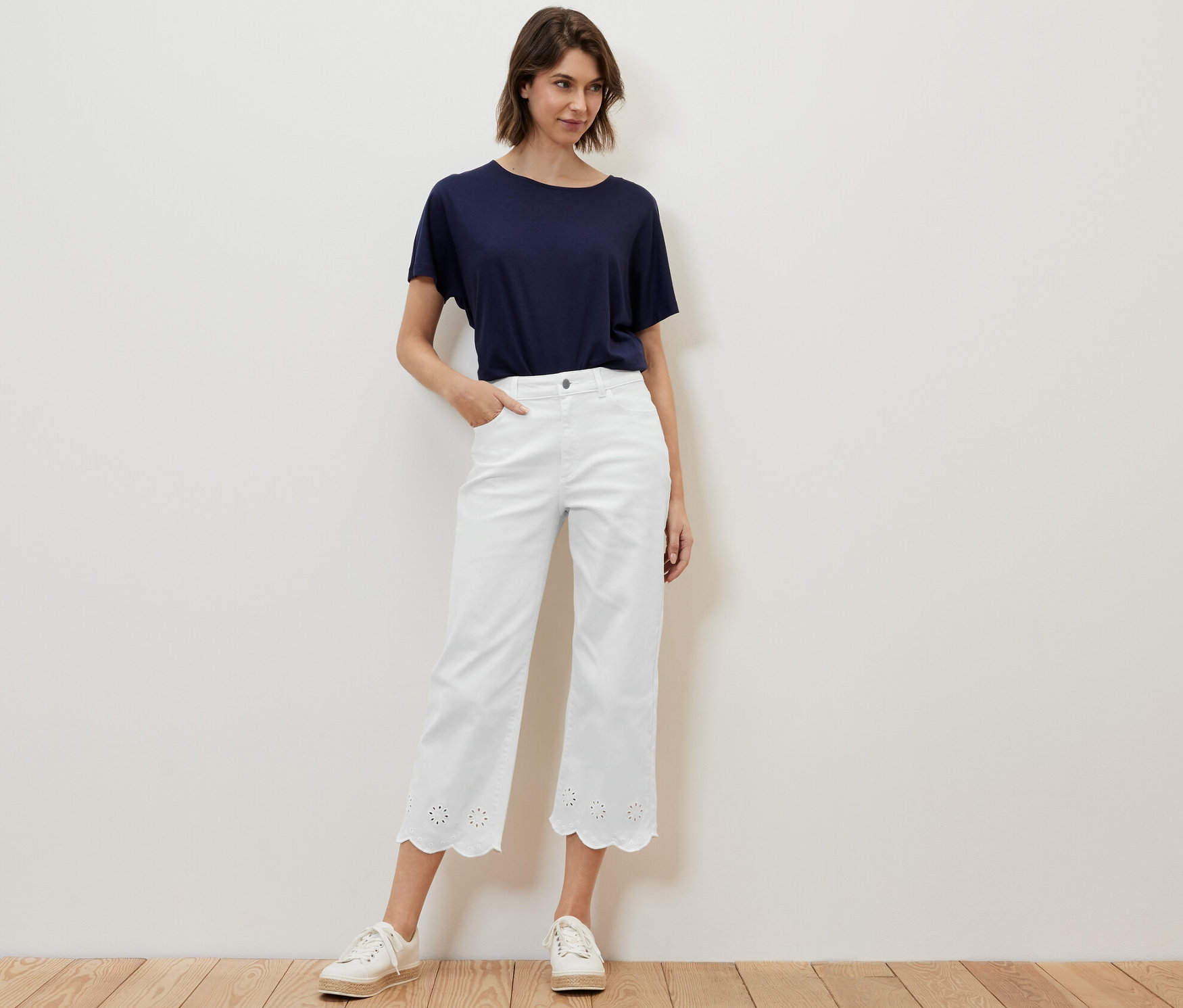 Frau posiert in weißen Jeans mit Lochstickerei und blauem T-Shirt.