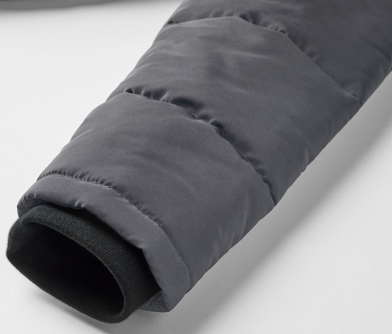 Detailansicht des Ärmels einer grauen Kinder-Steppjacke mit reflektierenden Elementen und einem schwarzen Bündchen.