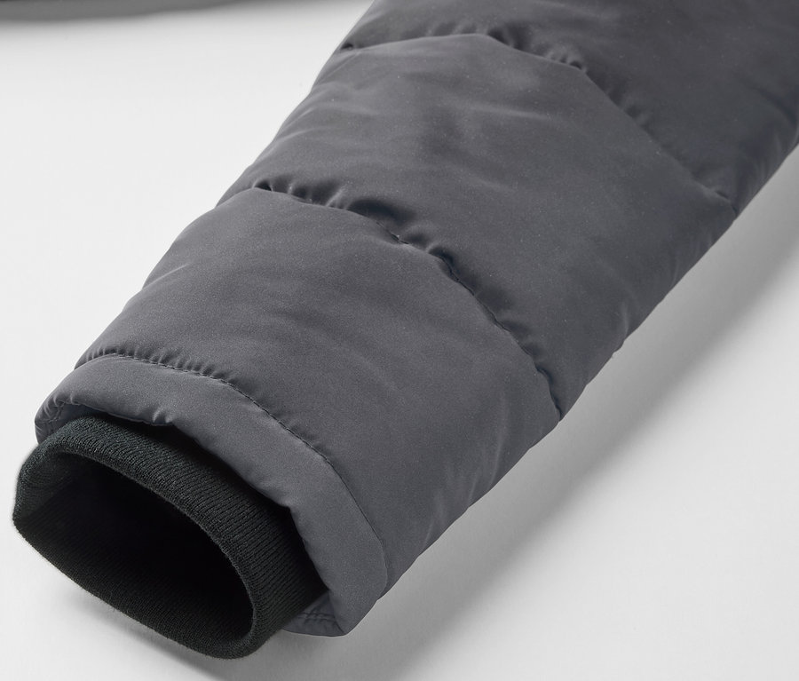 Detailansicht des Ärmels einer grauen Kinder-Steppjacke mit reflektierenden Elementen und einem schwarzen Bündchen.